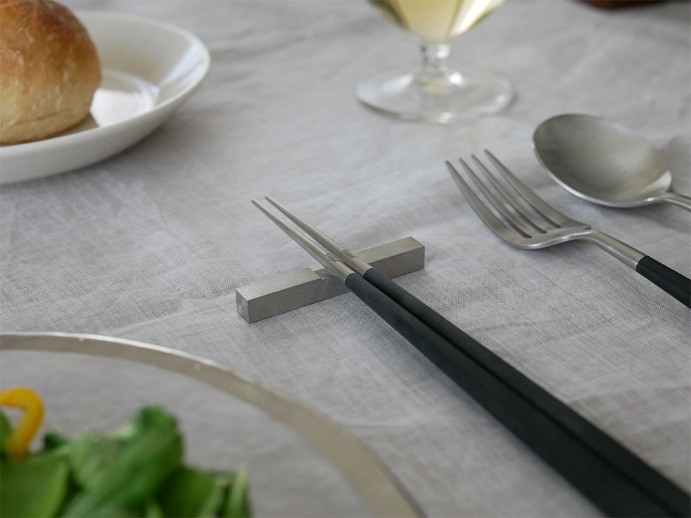 CutipolクチポールKUBEシリーズのブラックシルバー箸セット。天然樹脂と18-10ステンレス製の箸1膳と箸置きがテーブルに美しく配置されています。