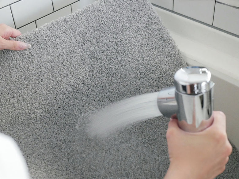 シルバー製の洗面台と蛇口、タオルや家庭用清掃用品が配置されたバスルーム