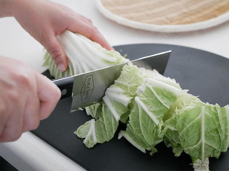 カッティングボードに新鮮な葉物野菜とクルシフェラス野菜が並べられ、TOOLSブランドのキッチンナイフが調理に使用されている様子