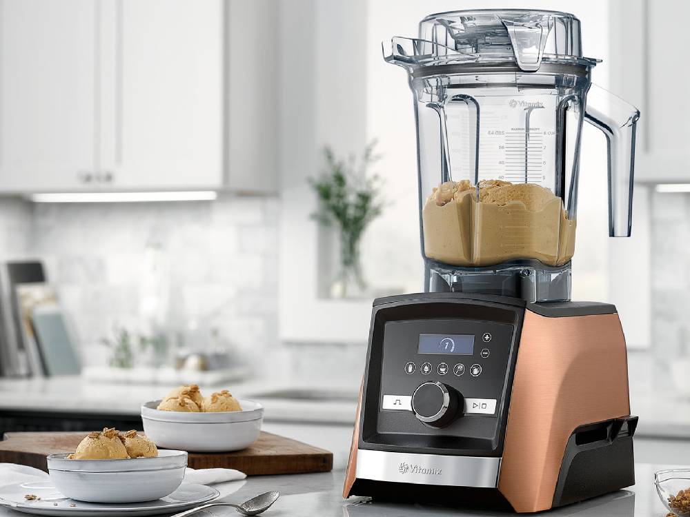 Vitamixのミキサーとコンテナがキッチンテーブルに配置され、食材や食器が周囲に並べられている様子