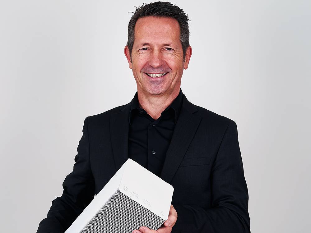 スタドラフォームのAnna BIGファンヒーターと共に笑顔で立つフォーマルなビジネススタイルの人物