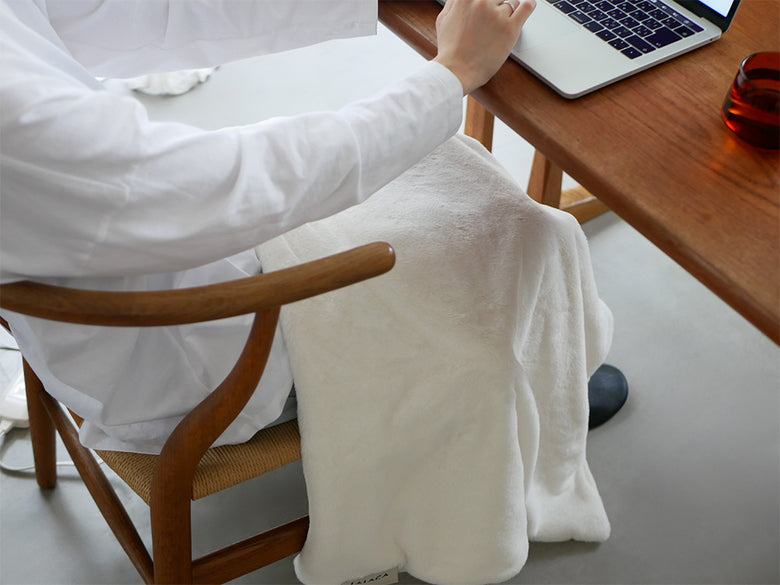 木製のデスクと椅子が配置された部屋の床に、ララカの洗えるなめらか素材のヒーターブランケットが広げられている様子。