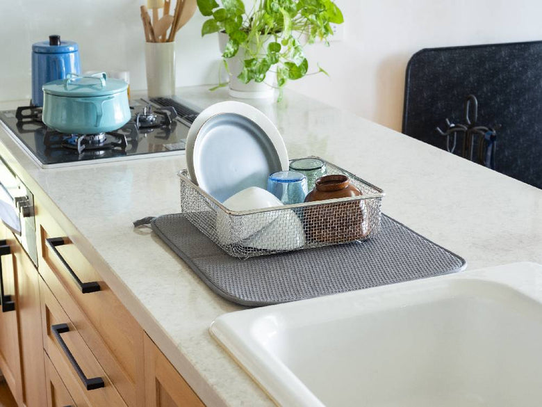 キッチンのカウンタートップに配置されたポリエステル製の水切りマット。シンクの近くに置かれ、食器や調理器具が整然と並べられている様子