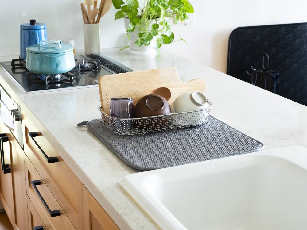 「bws SELECTION すっきり暮らす水切りマット」がキッチンカウンターに敷かれ、食器や調理器具が整然と配置されている様子