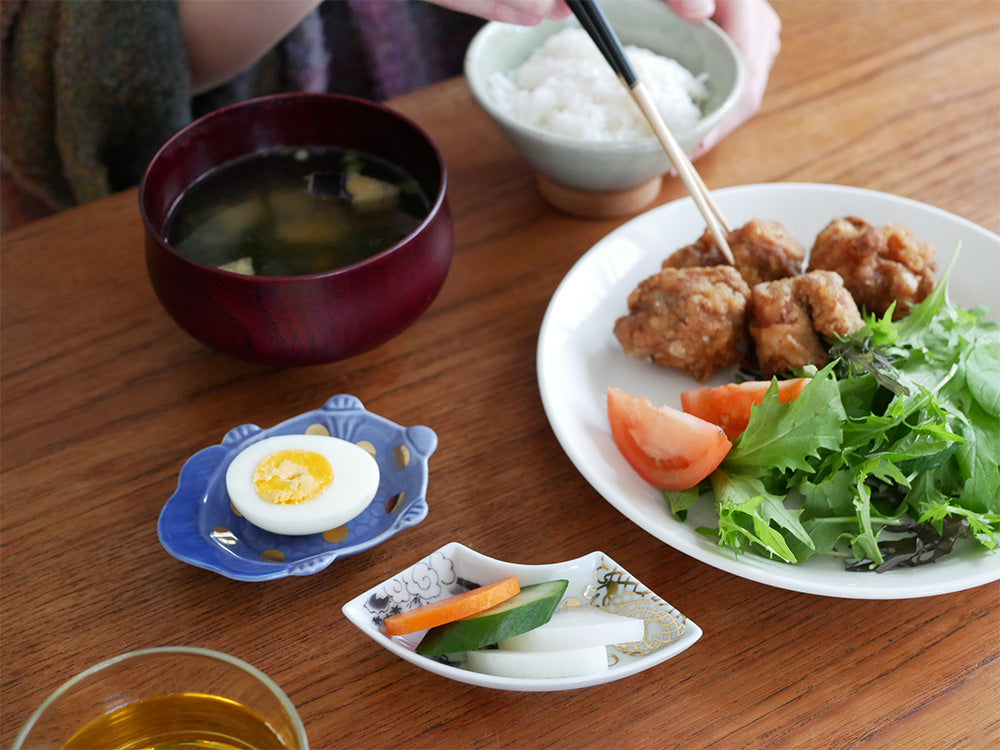 アマブロのMAMEシリーズに属する多種類の磁器製テーブルウェアが、食事と共にテーブルに美しく配置されている写真