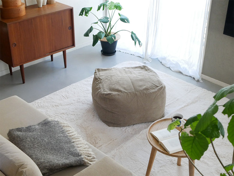 リビングルームに置かれたグレーのコーデュロイビーズクッションと椅子、自然素材の家具が快適な空間を演出しています