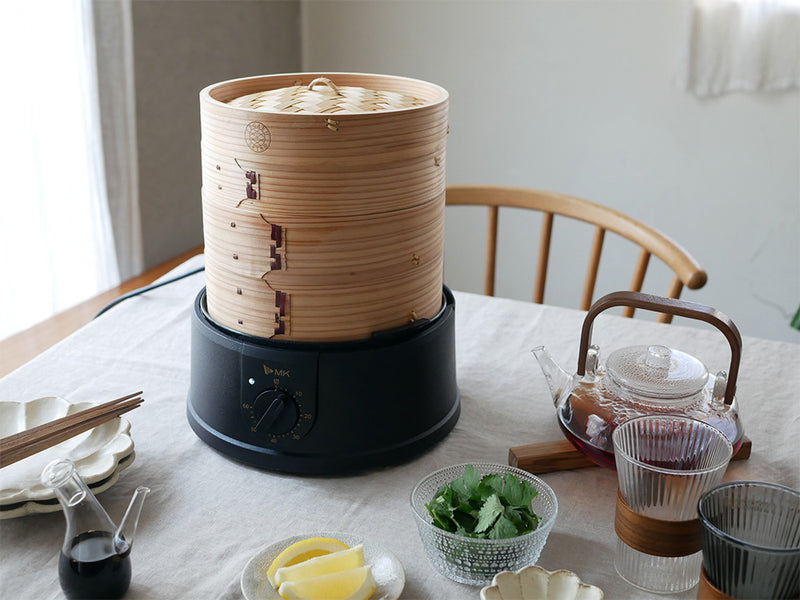 ほったらかし電気せいろの本体とせいろセット、蓋、延長輪が揃ってテーブルに配置されている様子