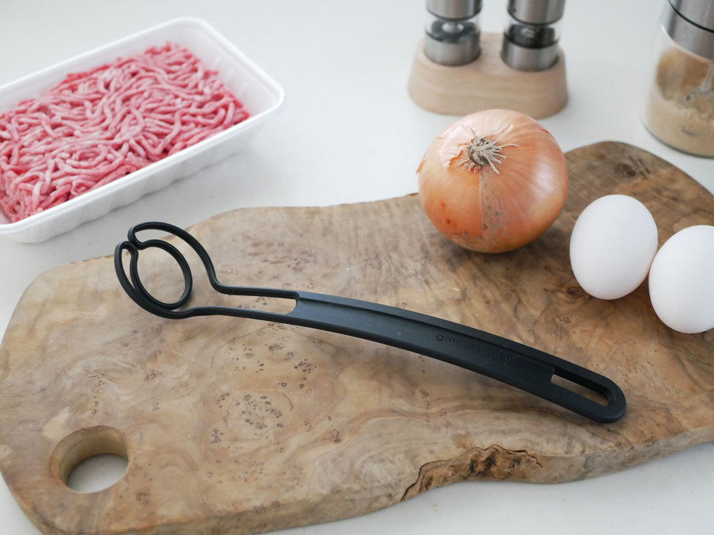 スウェーデン製マルチキッチンツール「オメガヴィスペン」がまな板上で肉や包丁などの調理器具と共に配置されている様子