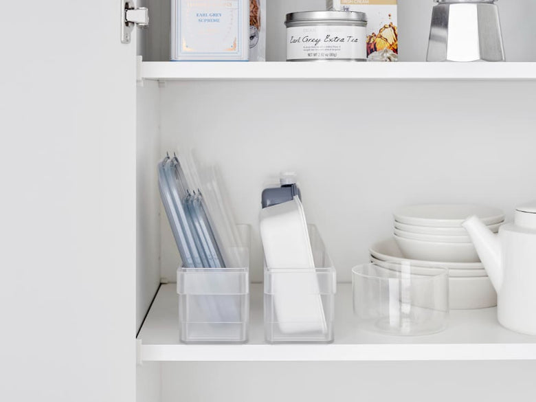 グレーのタワー型冷蔵庫用収納ケースが棚に整然と配置され、食器やキッチン用品を効率的に整理している様子