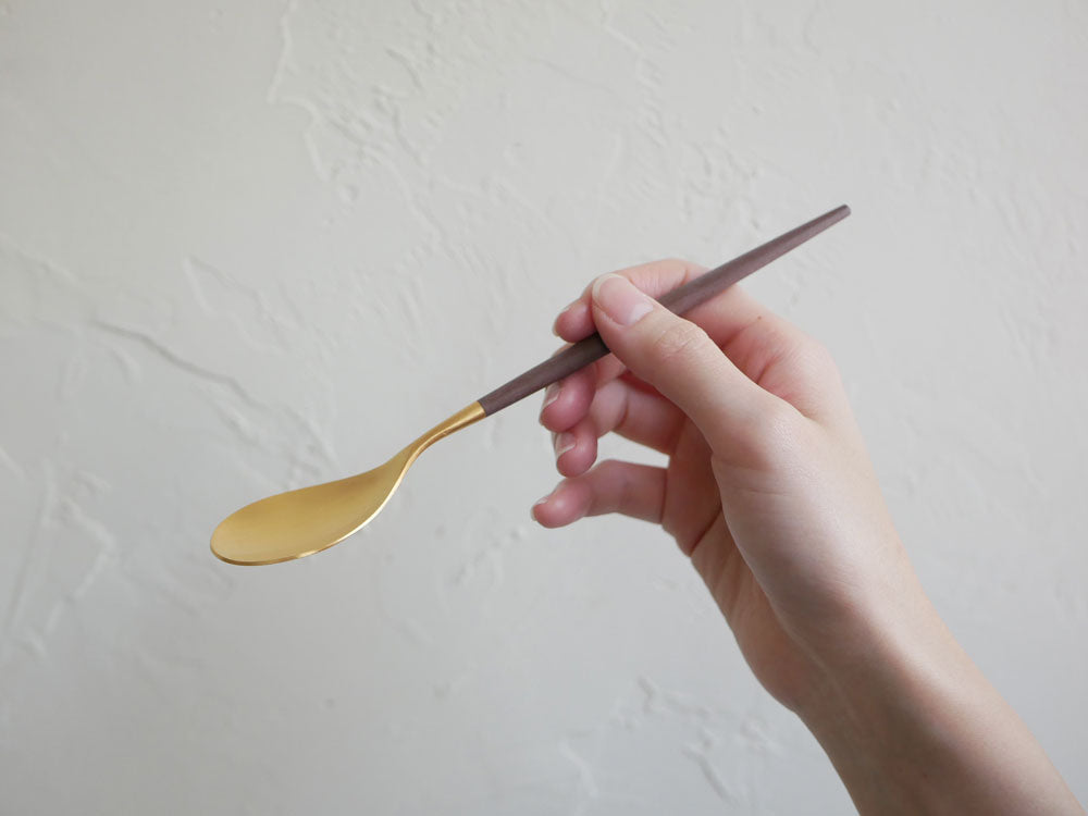 クチポールMIOのブラウンゴールドとグレーシルバーのディナー用フォーク、スプーン、ナイフが整然と並べられたテーブルセッティングの画像