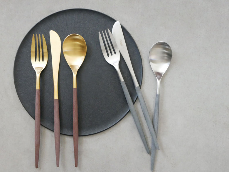 ブラウンゴールドとグレーシルバーのクチポールMIOカトラリーセットが木製のテーブル上に美しく配置されている様子