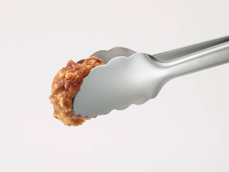 セレクト100の24cmステンレス製トングが肉や揚げ物を調理する際に使用されているキッチン用品とともに置かれている様子