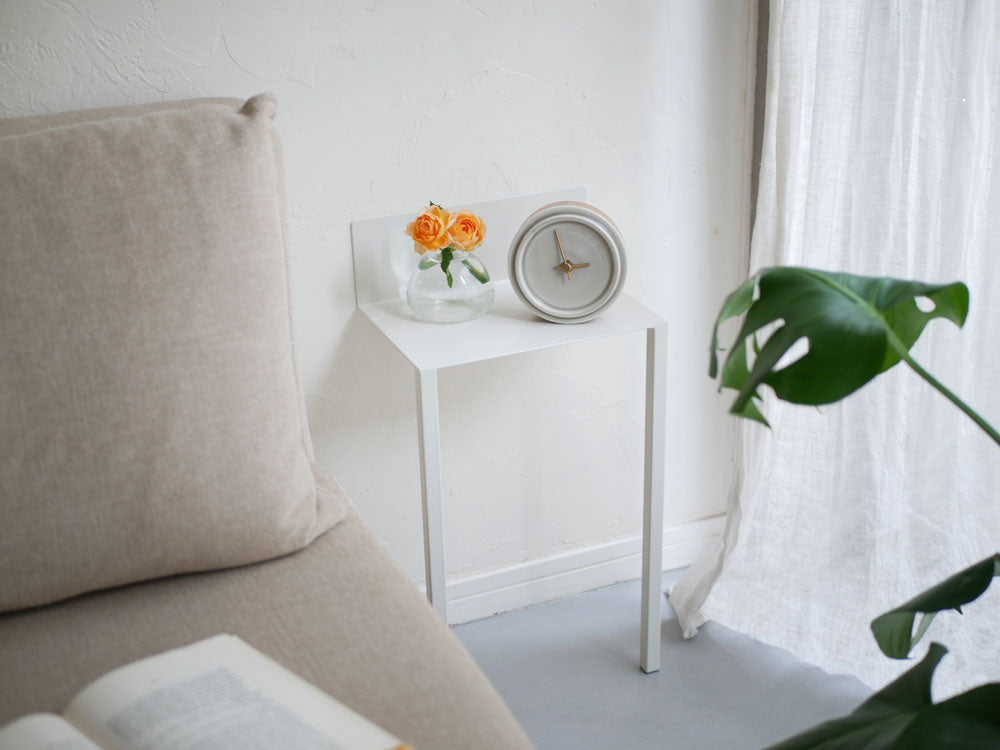 リビングルームに設置されたスチール製ウォールテーブルB5。テーブル上には花瓶と鉢植えがあり、ピンク色のクッションや装飾が周囲に配置されています。