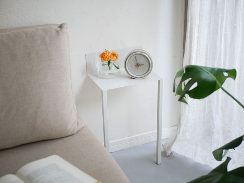 リビングルームに設置されたスチール製ウォールテーブルB5。テーブル上には花瓶と鉢植えがあり、ピンク色のクッションや装飾が周囲に配置されています。