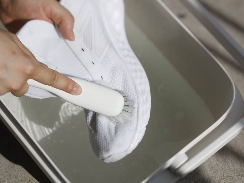 指と足でマーナのプラスチック製シューズブラシを使用して靴を清掃している様子