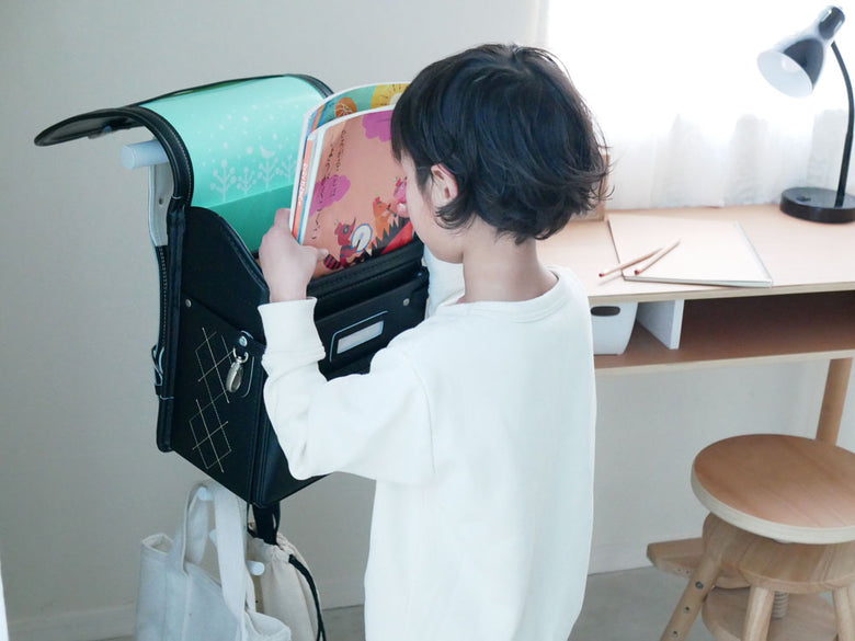 幼児が棚に設置されたスマートランドセルスタンドにランドセルを掛けている様子